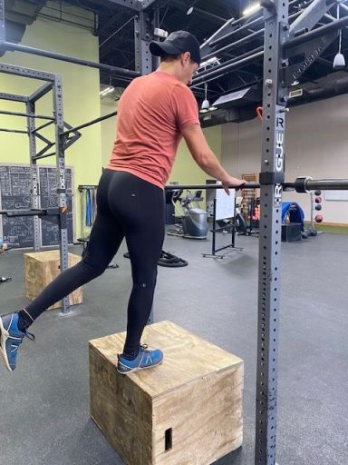 A person in workout gear balanced on a wooden box, preparing to exercise with a barbell.